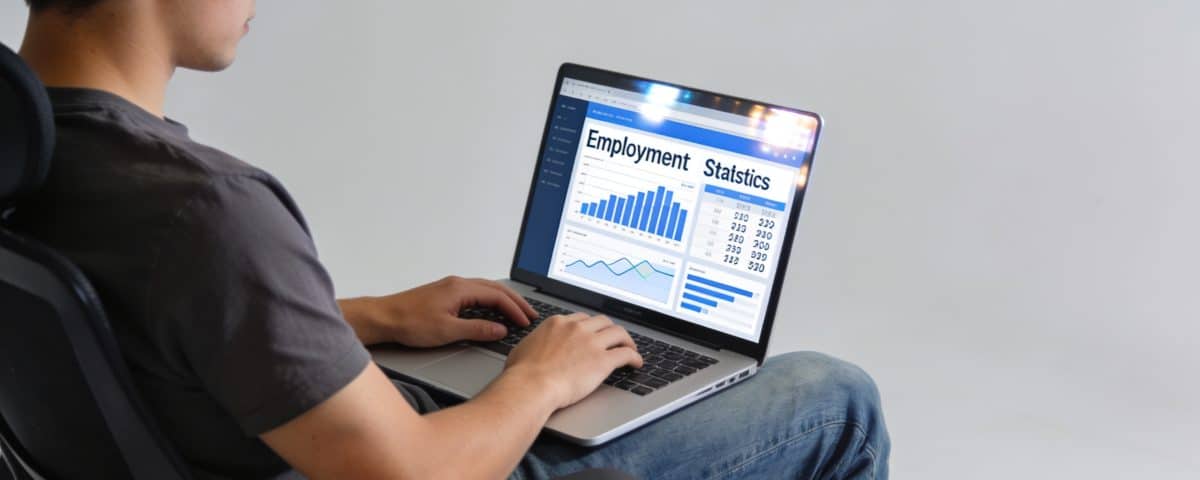 Jeune adulte assis devant ordinateur affichant statistiques emploi