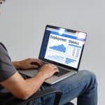 Jeune adulte assis devant ordinateur affichant statistiques emploi