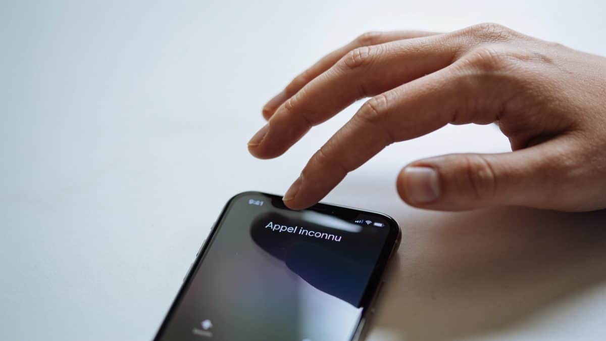 Smartphone affiche appel inconnu, main hesitante dessus