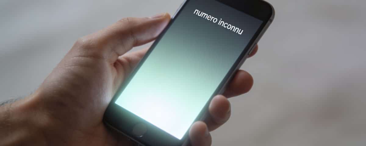 smartphone en main affichant numero inconnu ecran lumineux