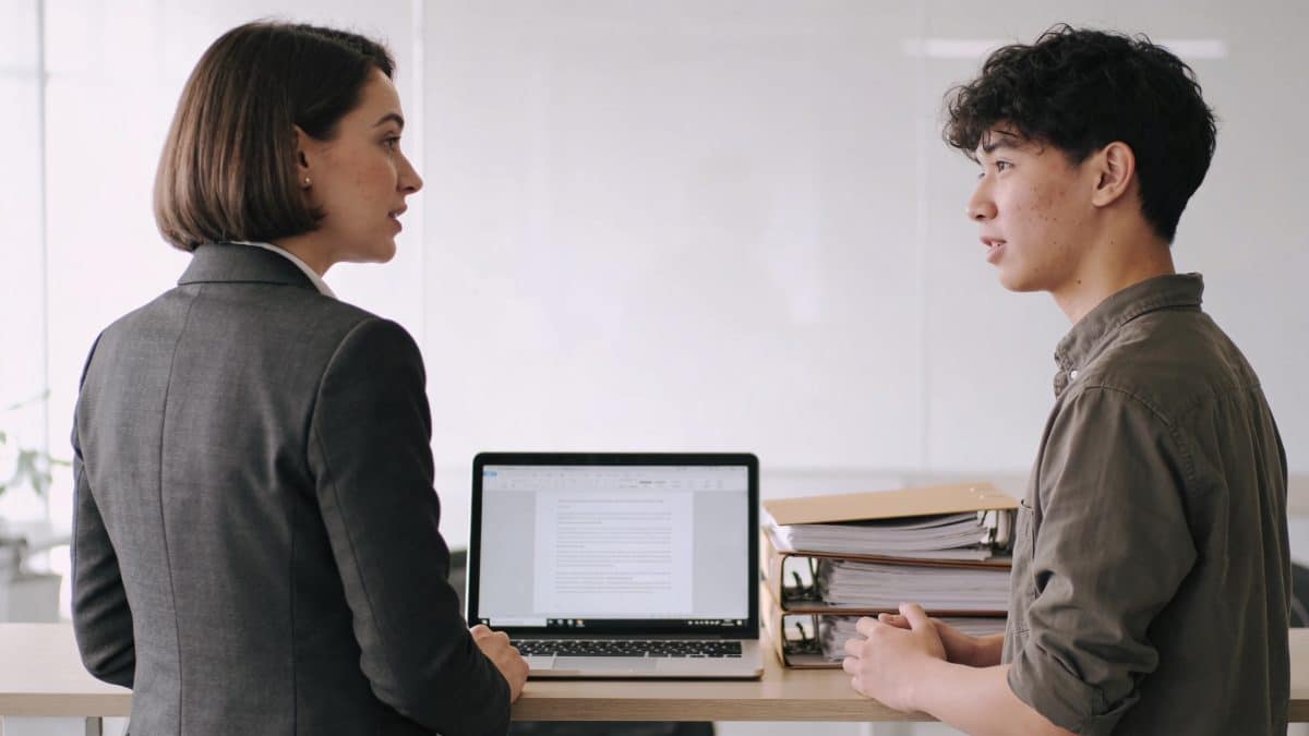 Superviseur et stagiaire discutant devant ordinateur et dossiers