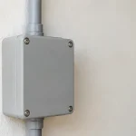 Boitier electrique gris fixe sur un mur blanc