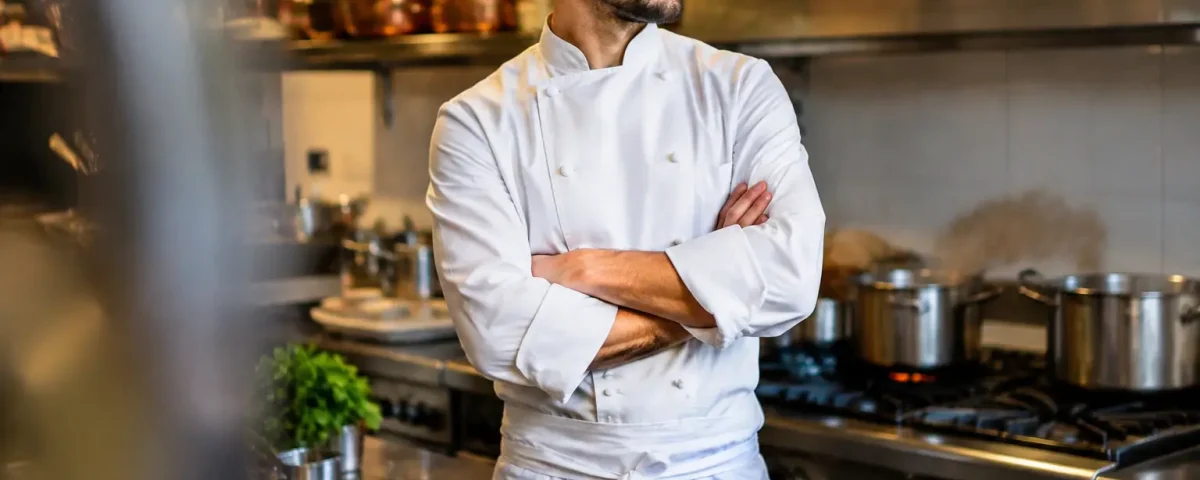 Cuisinier en veste blanche bras croises devant ses fourneaux