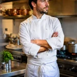 Cuisinier en veste blanche bras croises devant ses fourneaux