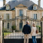 Grande demeure ancienne, deux adultes debout devant le portail