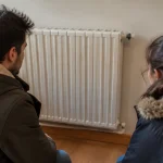 Deux adultes en manteau assis devant un radiateur eteint