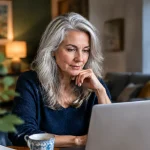 Femme aux cheveux gris assise devant un ordinateur portable