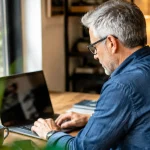 Homme aux cheveux gris assis devant un ordinateur portable