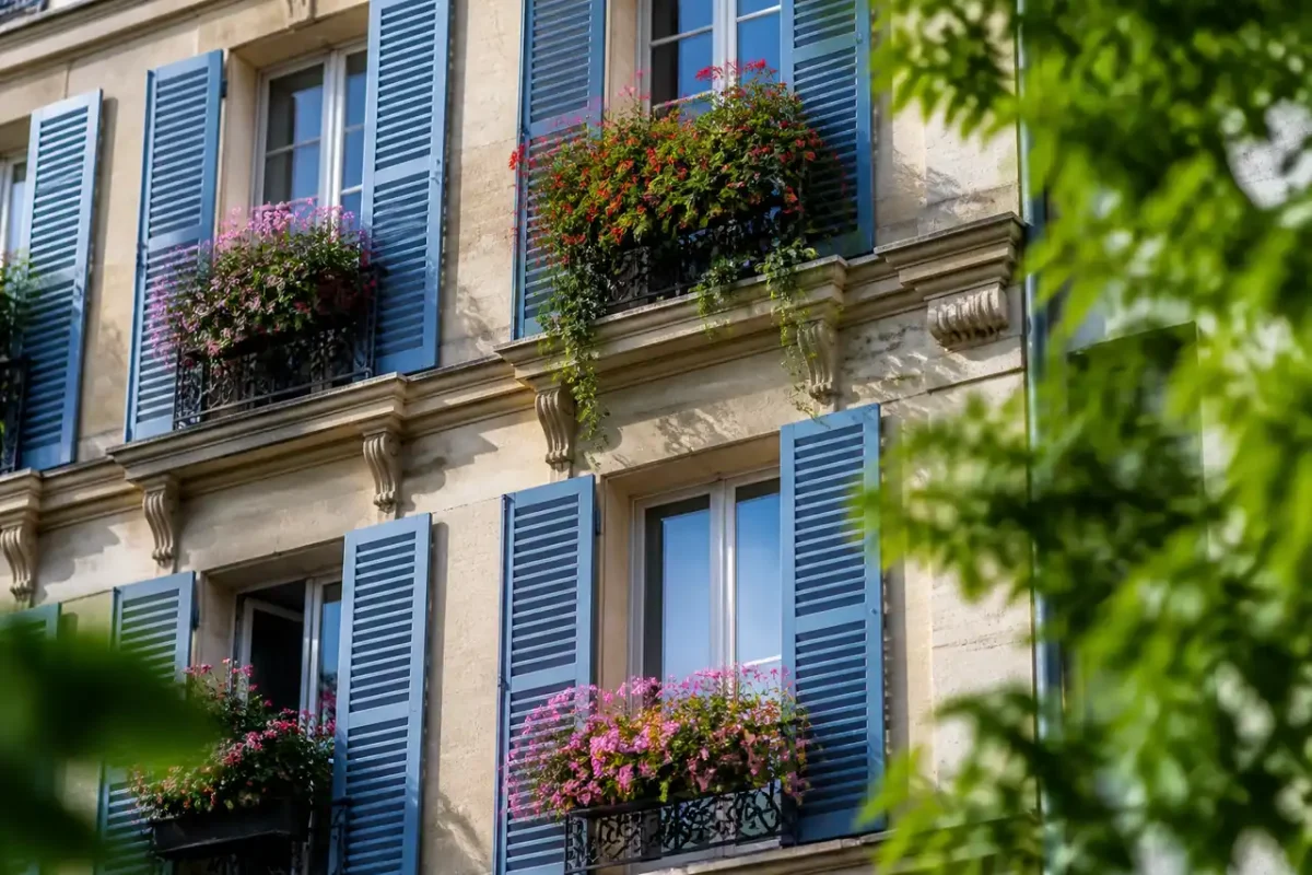 Facade immeuble parisien avec balcons fleuris et volets bleus