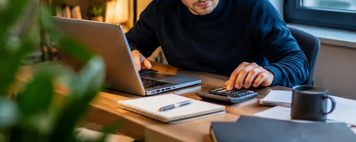 Jeune homme assis devant un ordinateur et une calculatrice