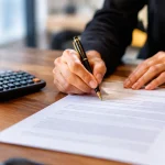 Main signant un contrat papier pres dune calculatrice