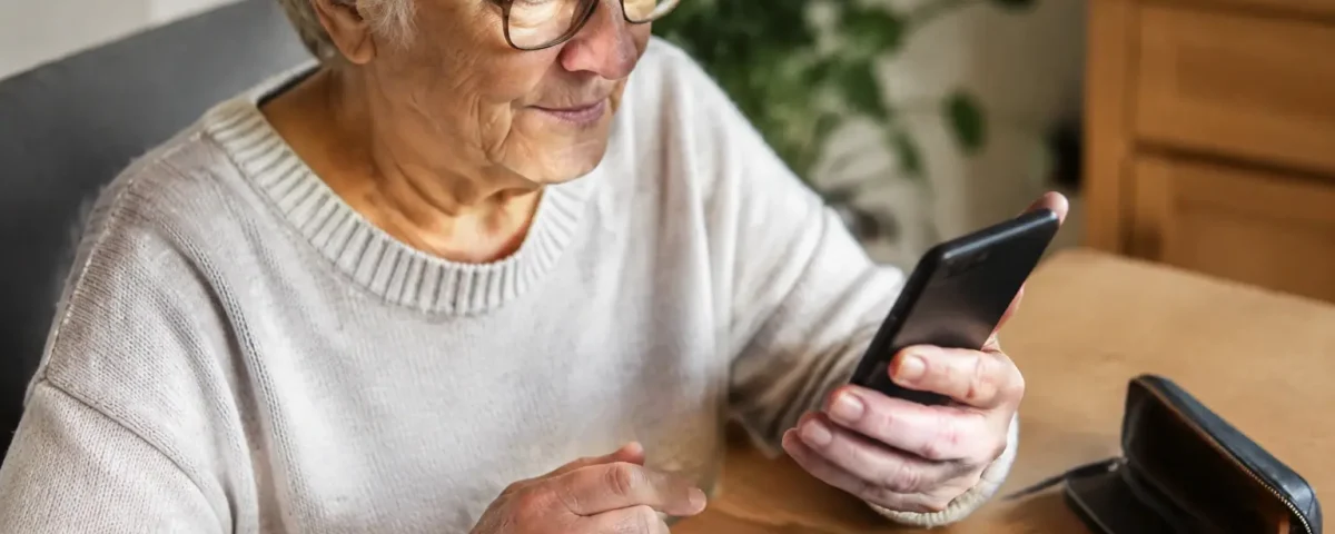Retraitee assise tenant un smartphone pres de pieces