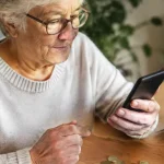 Retraitee assise tenant un smartphone pres de pieces